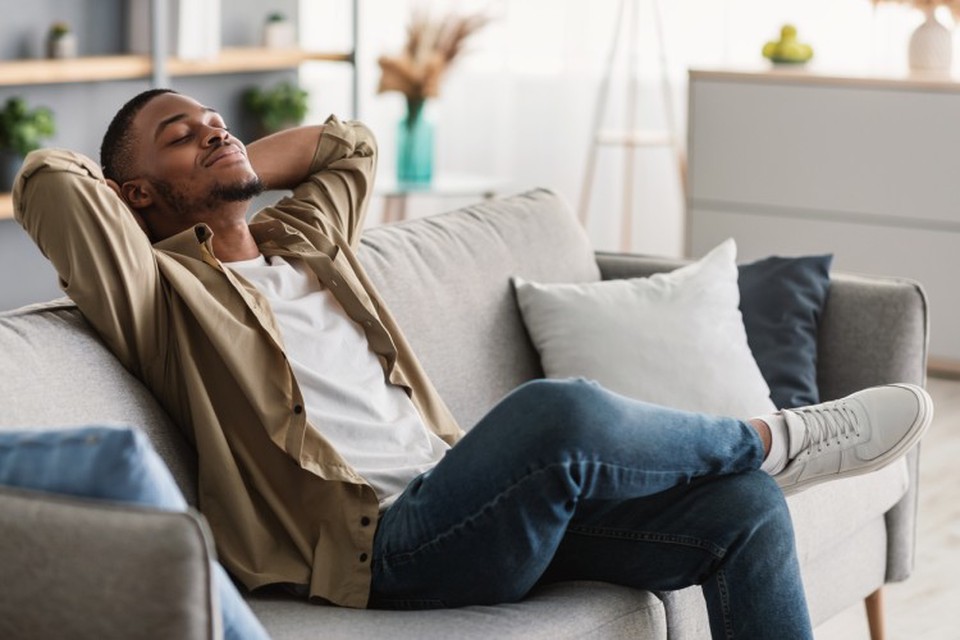 A person relaxes on a couch with their eyes closed.