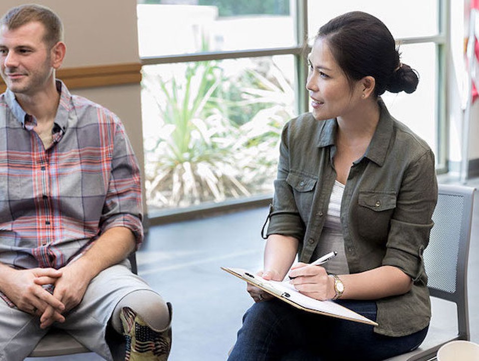 Social worker sits in a circle with other individuals, facilitating a group therapy session. 