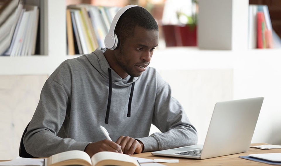 A man surrounded by books completes online courses using a laptop.