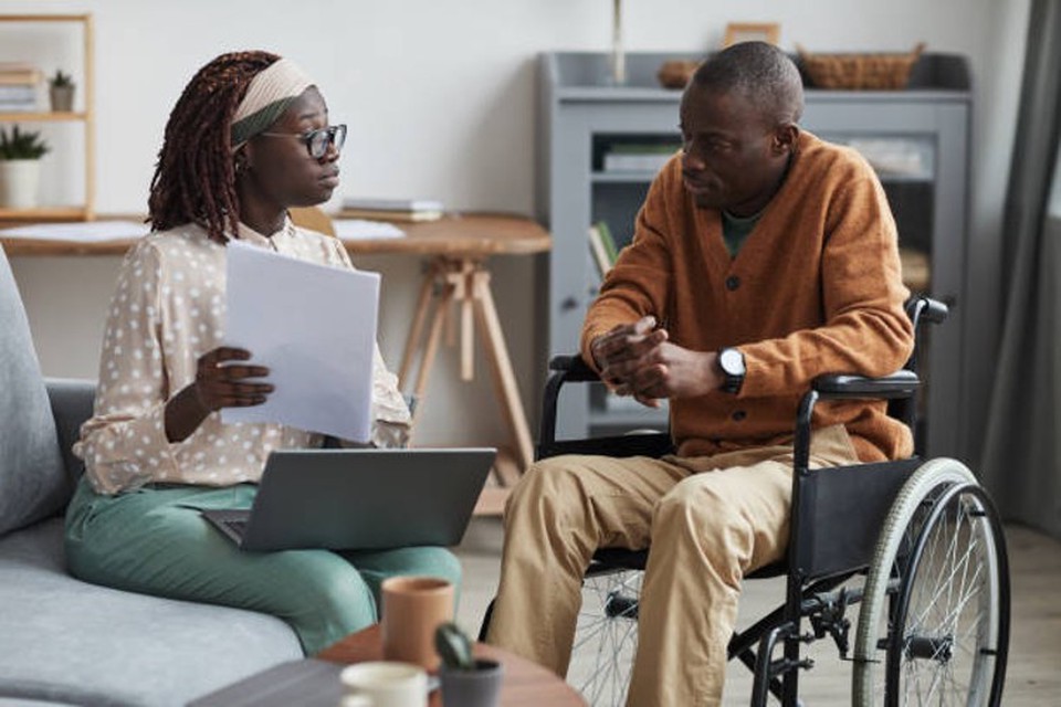 A social worker meets with a client seated in a wheelchair.
