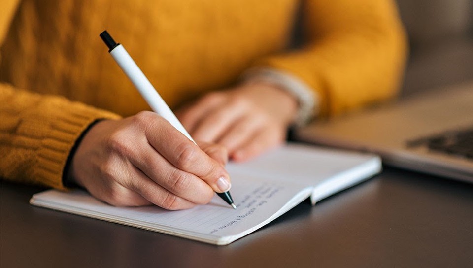 A hand writes with a pen on a notebook