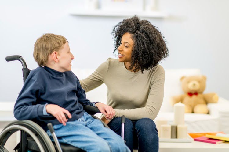 A social worker talks with a young client seated in a wheelchair.