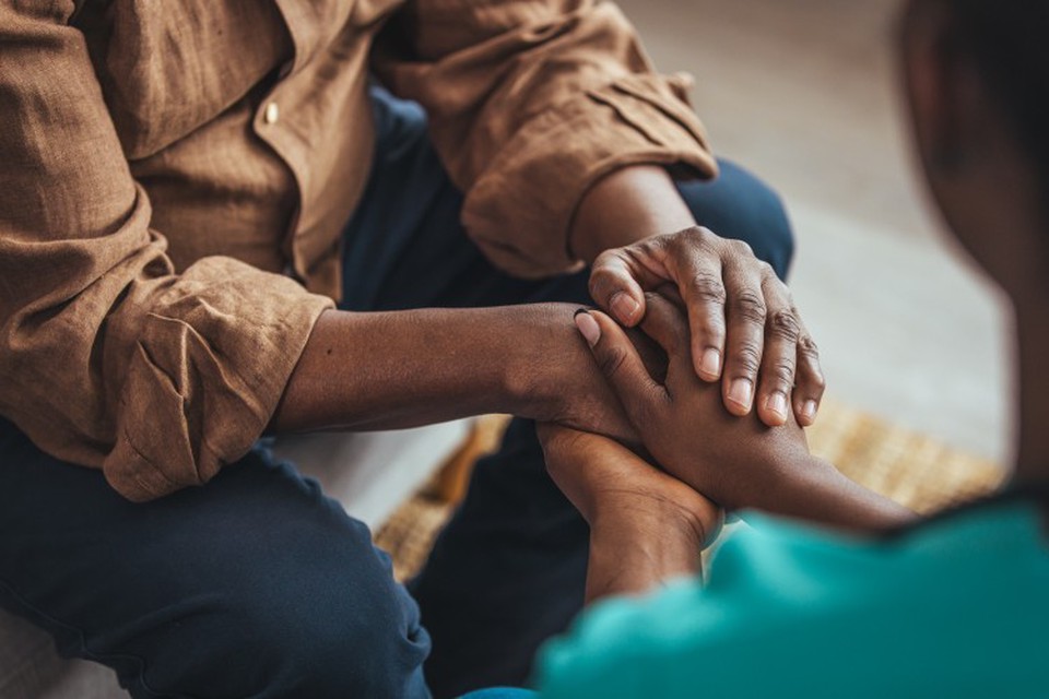 A social worker sits across from a client and holds their hands.