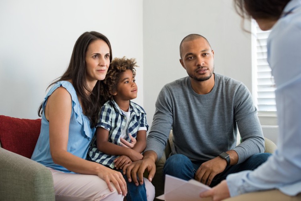 A couple seated on a couch with a young child speaks to an adoption social worker.