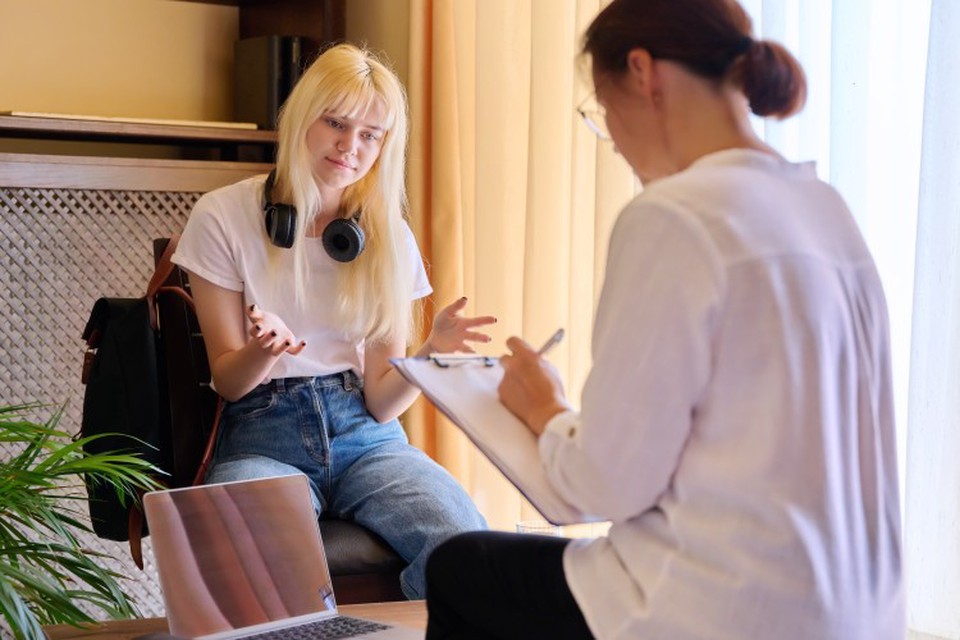 A social worker takes notes on a clipboard while meeting with a teenager.