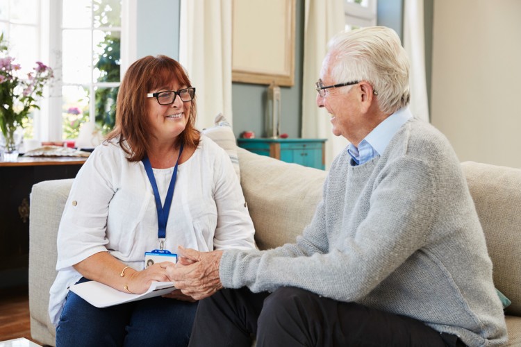 A smiling social worker visits an older person in their home.